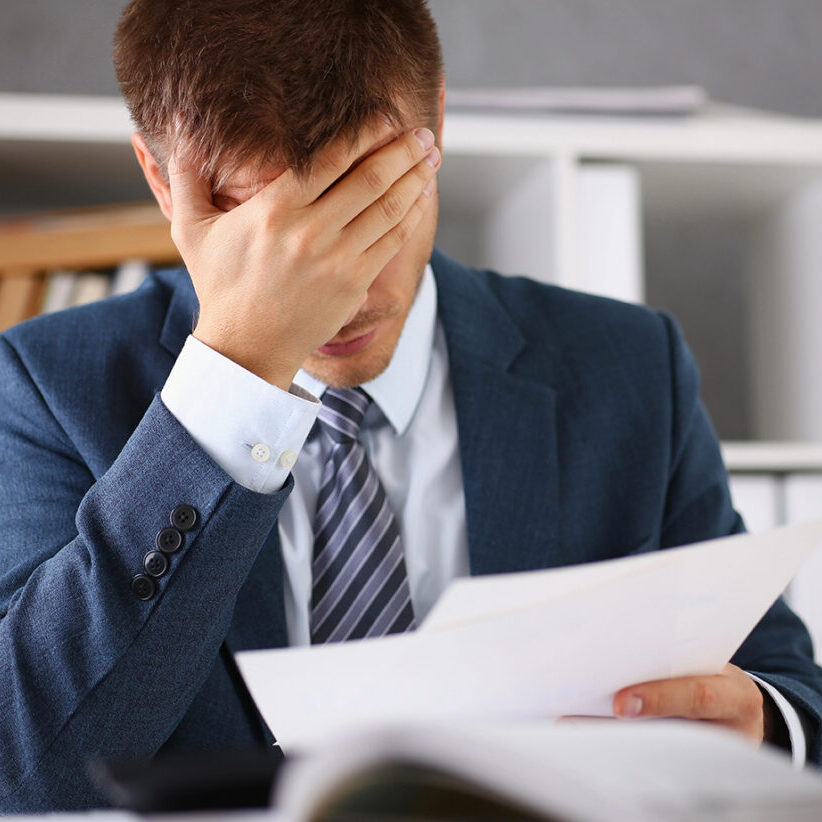 A man experiences stress and a headache in the workplace experiences negative emotions from paper red tape trouble personality disorder and career growth lack of knowledge