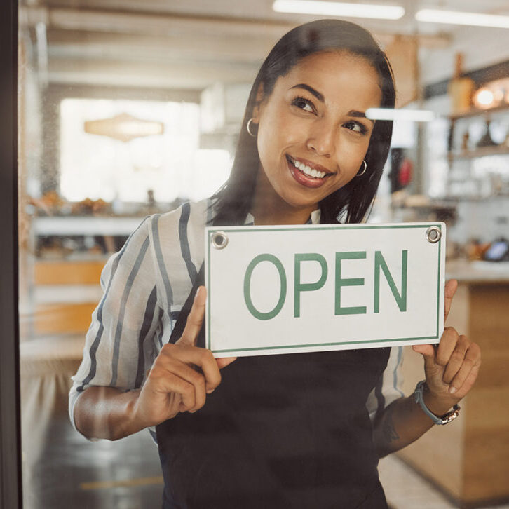 Businesswoman hanging an open sign in her shop door. Business owner waiting for customers in her store entrance. Boss advertising that her cafe is open for business. Ready and open for service.