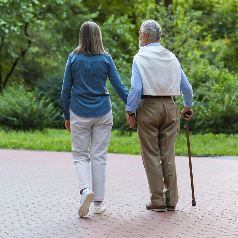Senior man with walking cane and mature woman outdoors, back view. Space for text