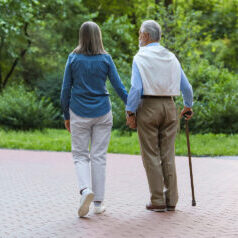 Senior man with walking cane and mature woman outdoors, back view. Space for text