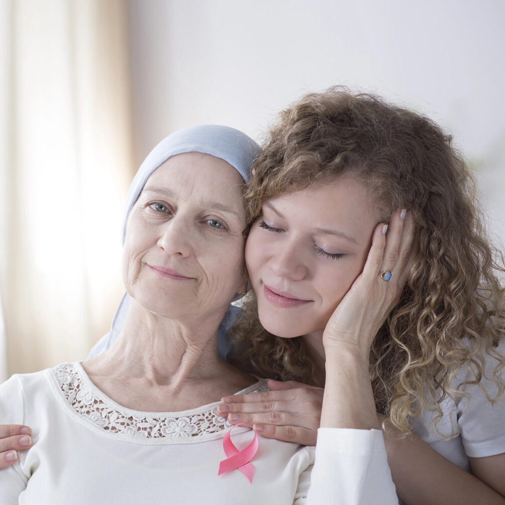 Smiling daughter hugging her mother with cancer in a white room